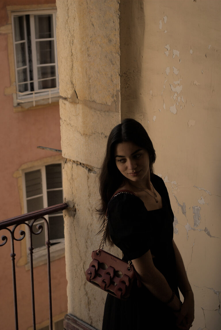 Photo de mode avec une mannequin portant un sac et une robe noire, près d'un balcon