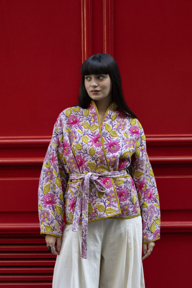 Photo de mode avec une mannequin de face portant une veste à fleurs, le tout avec un mur totalement rouge